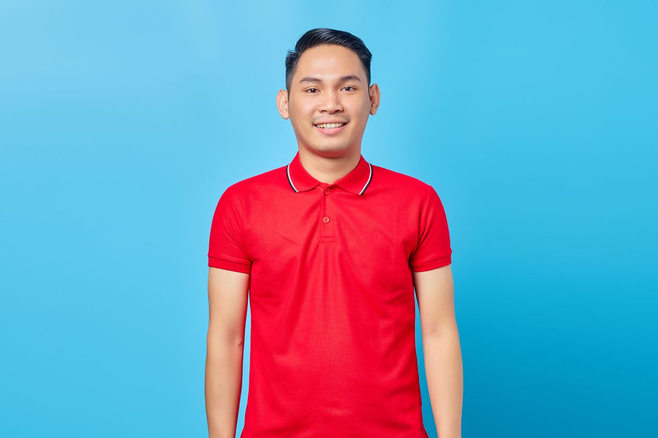 journey Cheerful young adult man wearing a red polo shirt, posing against a bright blue backdrop.