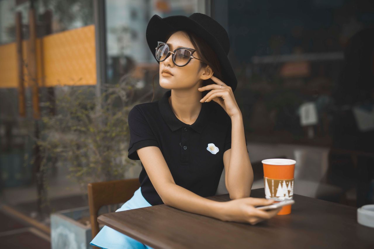 services-04 Chic woman in black hat and sunglasses sitting at a cafe with a coffee cup, embodying casual elegance.