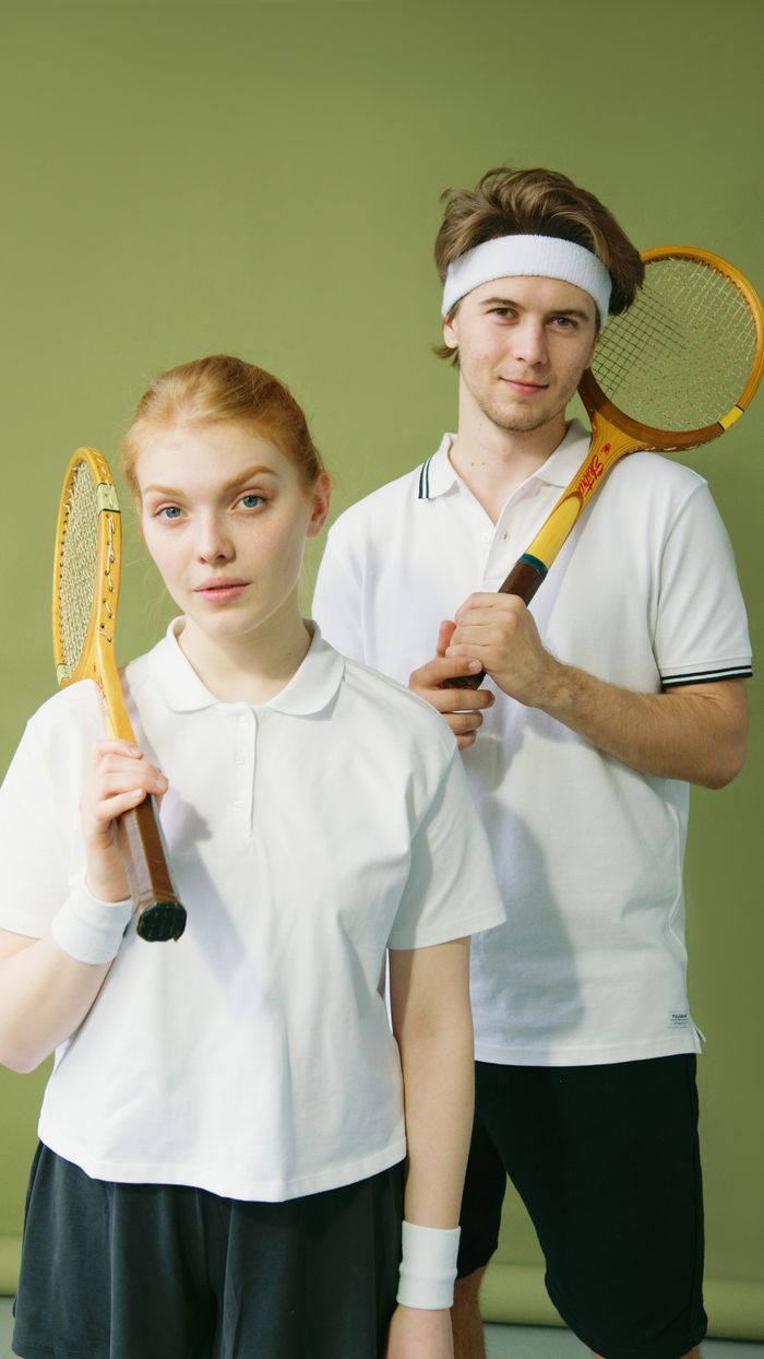 services-02 Young male and female squash players posing with rackets against a green background.